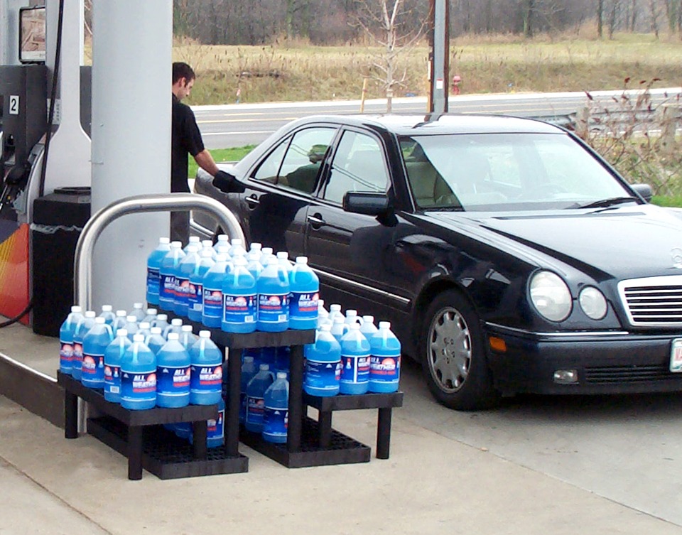 a three-tier plastic display holding antifreeze at a gas station pump